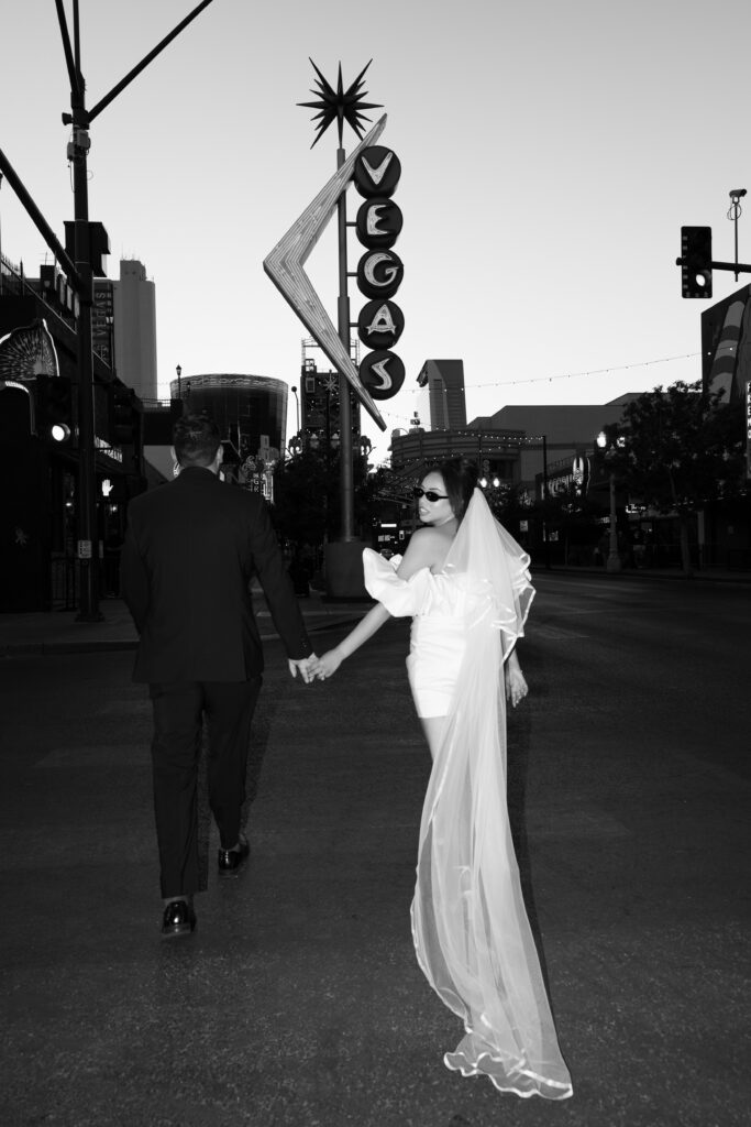 Black and white photo of a bride and groom walking downtown Las Vegas in front of the vintage neon sign