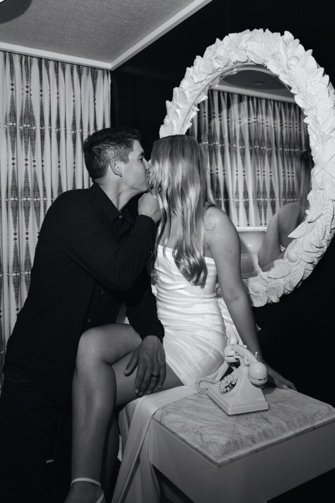 Black and white photo of a bride and groom kissing next to an old dial phone for their Encore Las Vegas wedding portraits