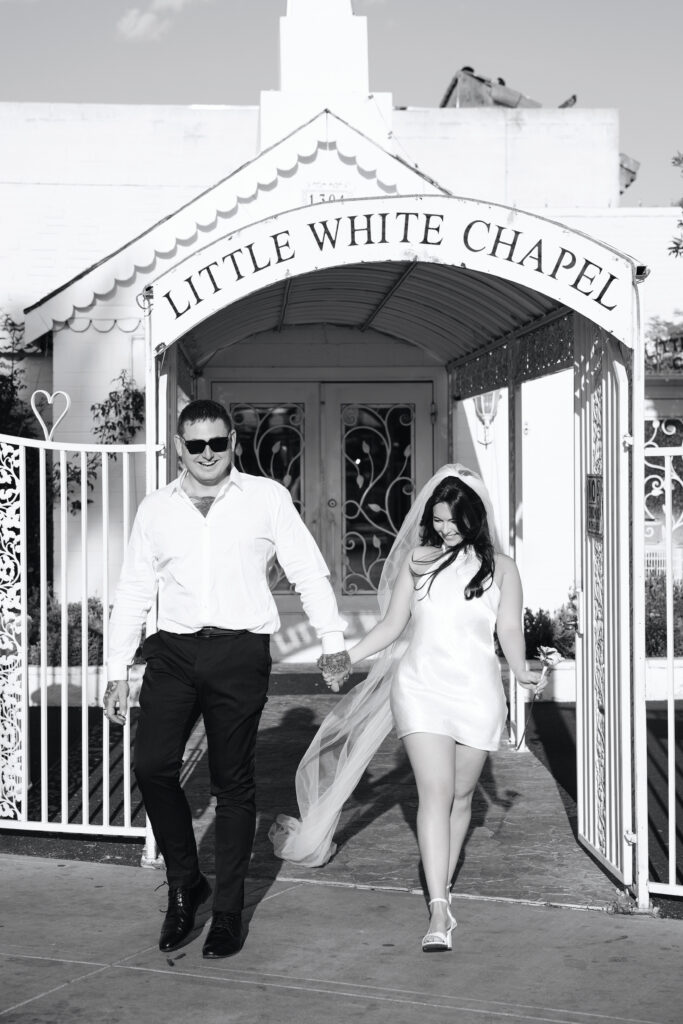 Black and white photo of a bride and groom walking out of The Little White Wedding Chapel Las Vegas