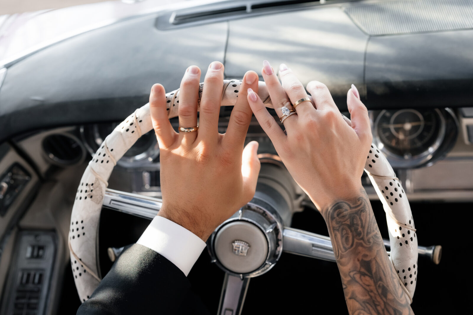 Bride and groom showing off their rings as they hold onto a steering wheel