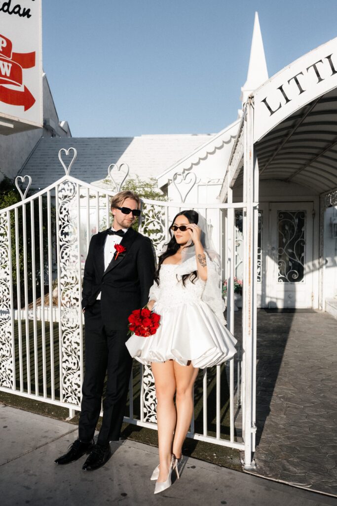 Bride and groom posing outside of The Little White Wedding Chapel in Las Vegas with sunglasses on.