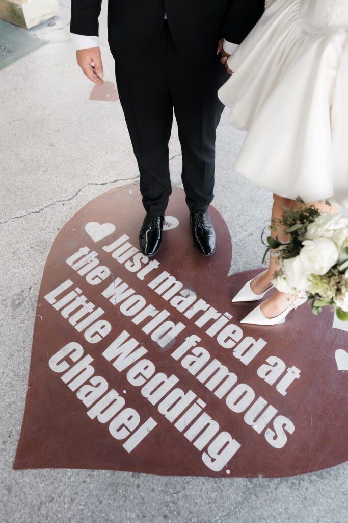 Couple posing on top of a red heart that says "Just married at the world famous Little Wedding Chapel".