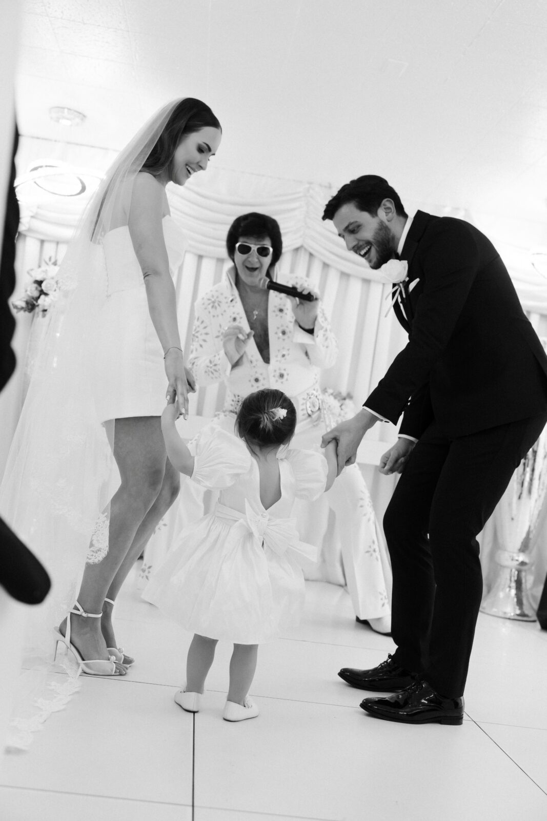 Black and white photo of a bride, groom, and their young daughter dancing during their Las Vegas Elvis wedding ceremony.