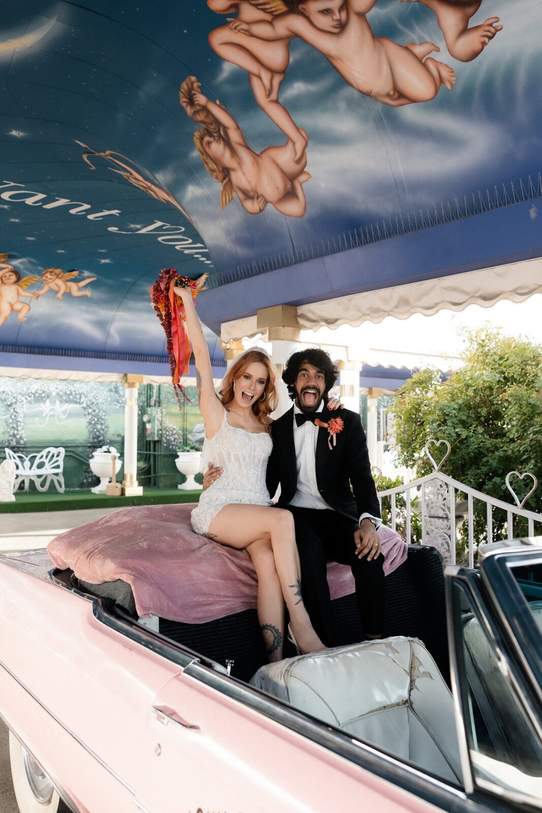 Bride and groom posing in the iconic Pink Cadillac at The Little White Wedding Chapel.