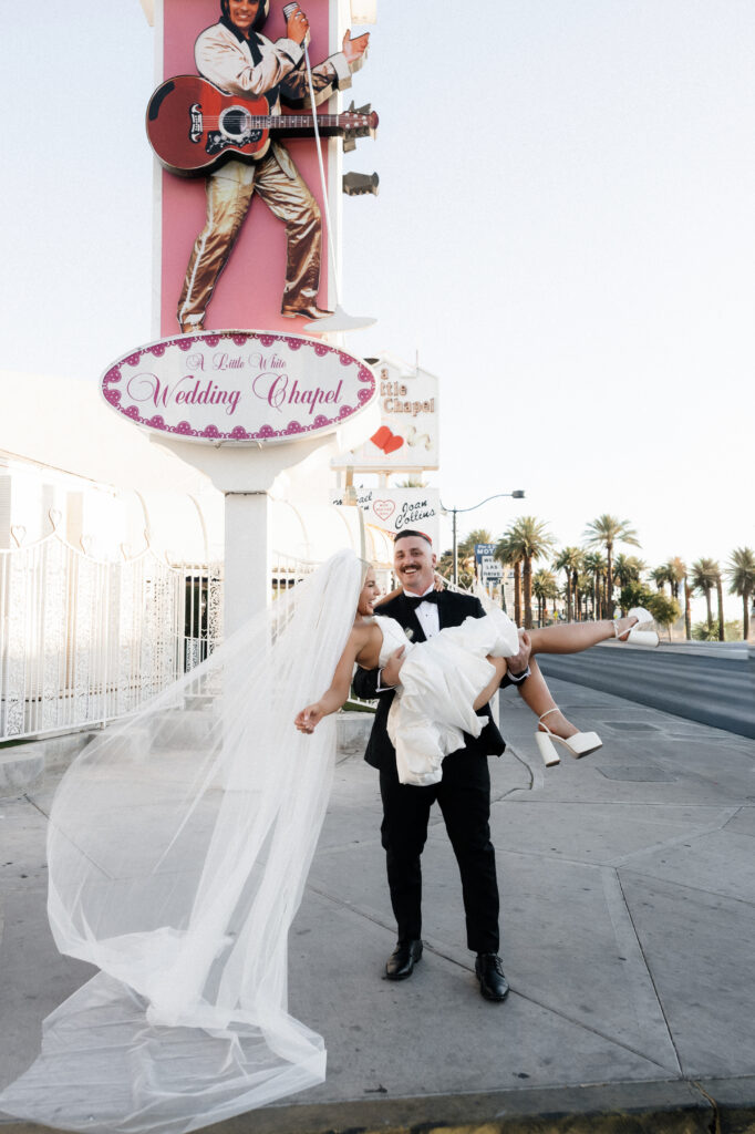 Groom holding his bride in his arms in front of The Little White Wedding Chapel in Las Vegas.