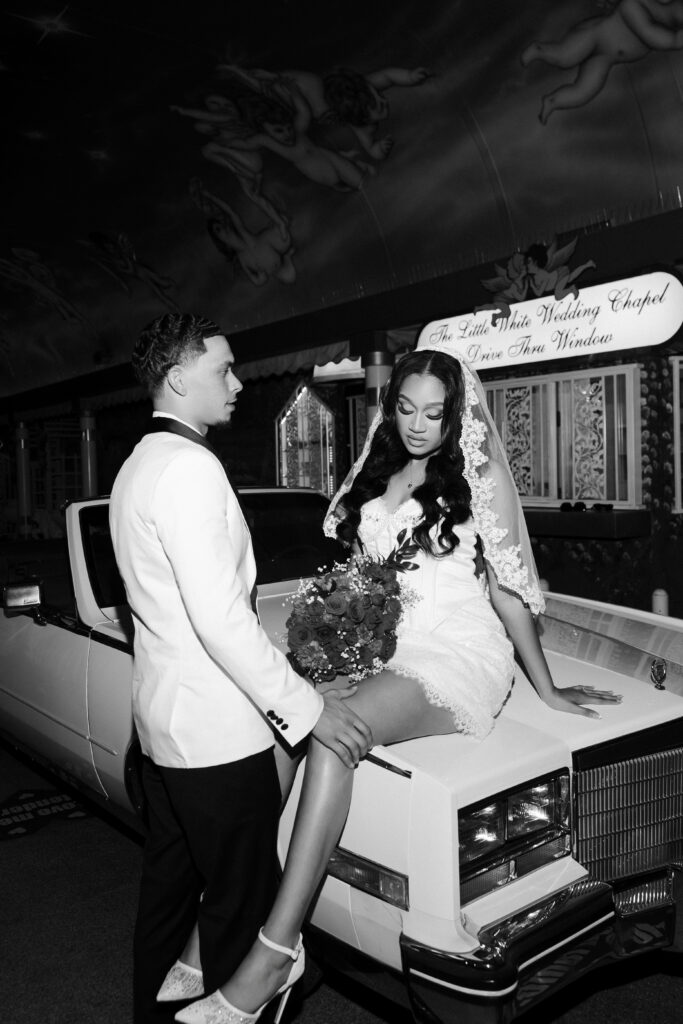 Bride and groom posing with the Risky Ride for their Tunnel of Love Drive-Thru Ceremony at The Little White Wedding Chapel.