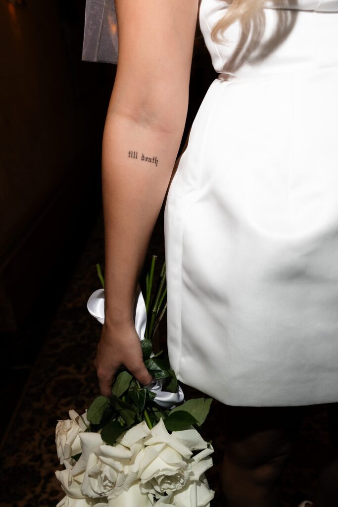 Close up shot of a bride holding her wedding bouquet and showcasing her tattoo that says till death