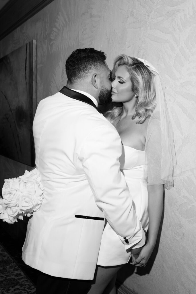 Black and white photo of a bride and groom kissing in a hotel hallway