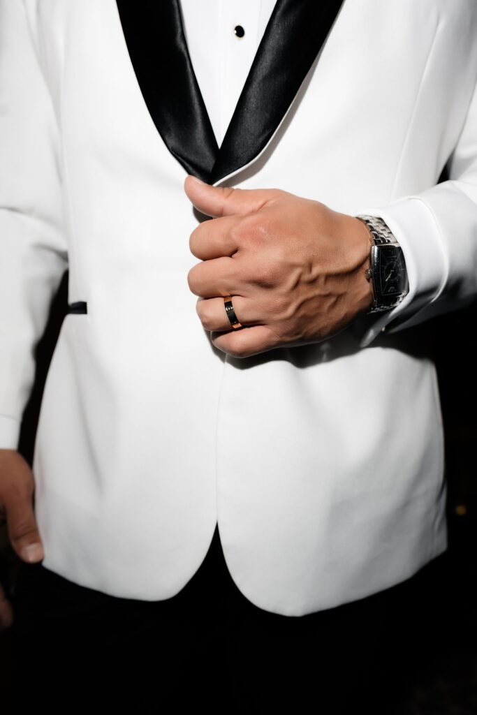 Close up shot of a grooms white suit while wearing his wedding band and watch