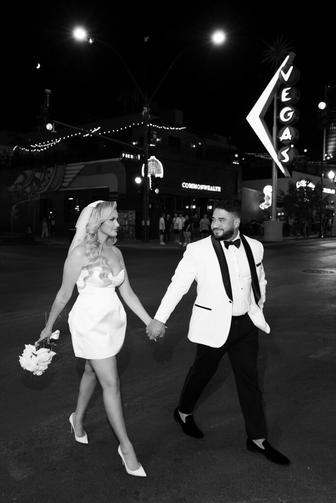 Black and white photo of a bride and groom walking down Fremont Street during their Las Vegas elopement portraits 