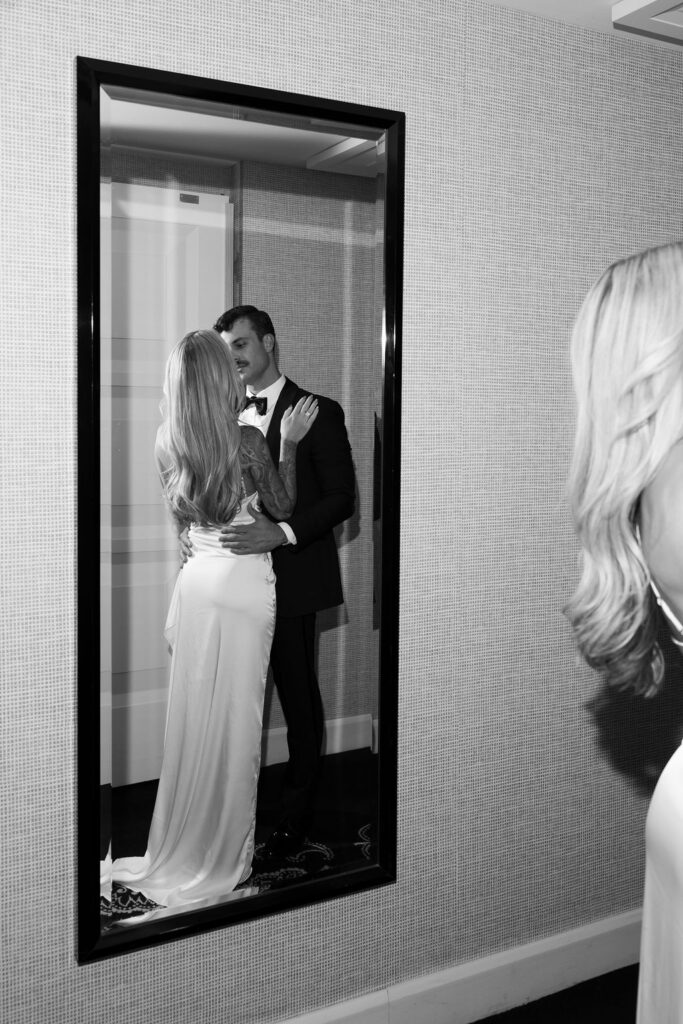 Black and white photo of a bride and groom kissing in their hotel suite mirror