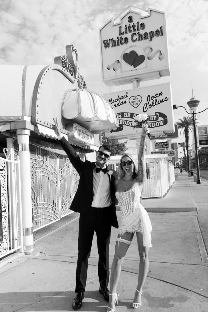 Black and white photo of a bride and groom posing in front of The Little White Wedding Chapel