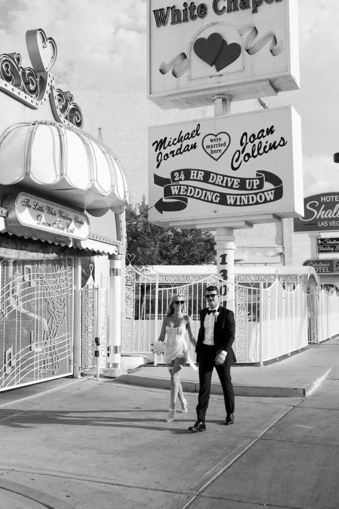 Black and white elopement photo of bride and groom walking in front of the Little White Wedding Chapel in Las Vegas