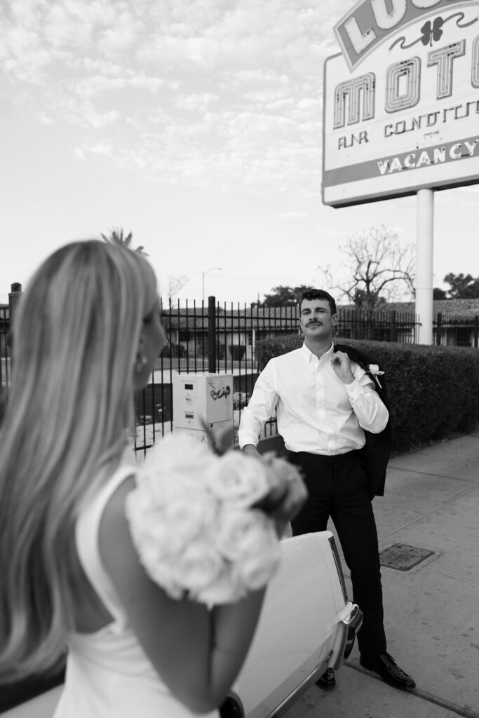 Black and white photo of a bride and groom posing with a classic car