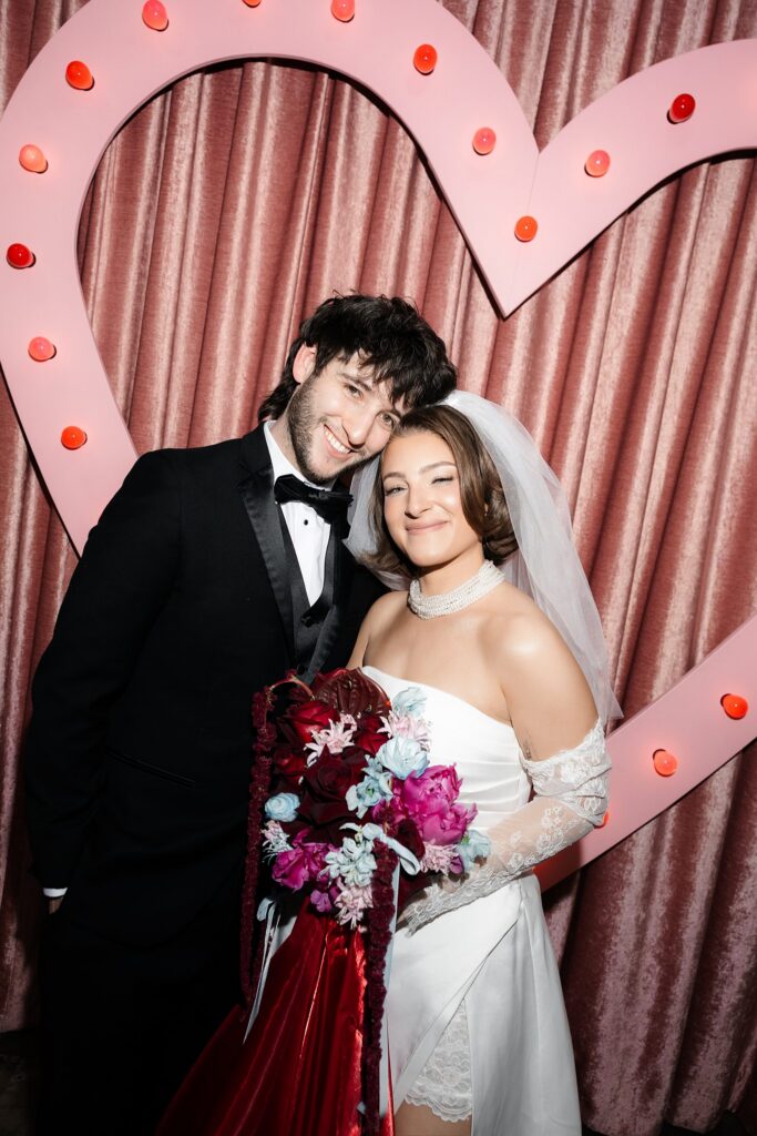 Bride and groom posing in front of the pink heart at Sure Thing Chapel in Las Vegas.
