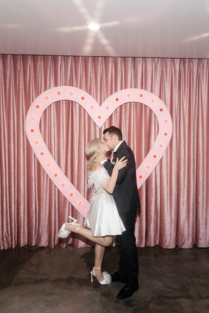 Bride and groom kissing in front of the pink heart at Sure Thing Chapel.