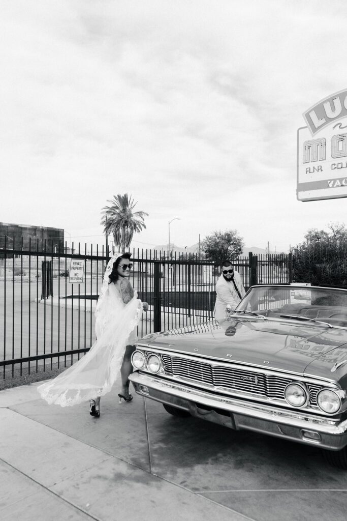 Black and white photo of a couple posing with the classic car at Sure Thing Chapel in Las Vegas.