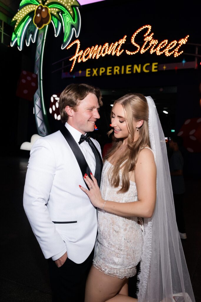 Bride and groom walking in front of the Fremont Street Experience sign in Las Vegas at night.