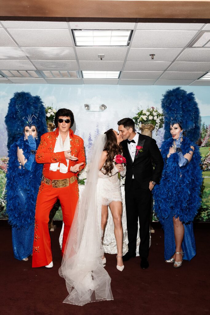 Bride and groom kissing and posing with Elvis and Showgirls after their Chapel Amore Las Vegas wedding.