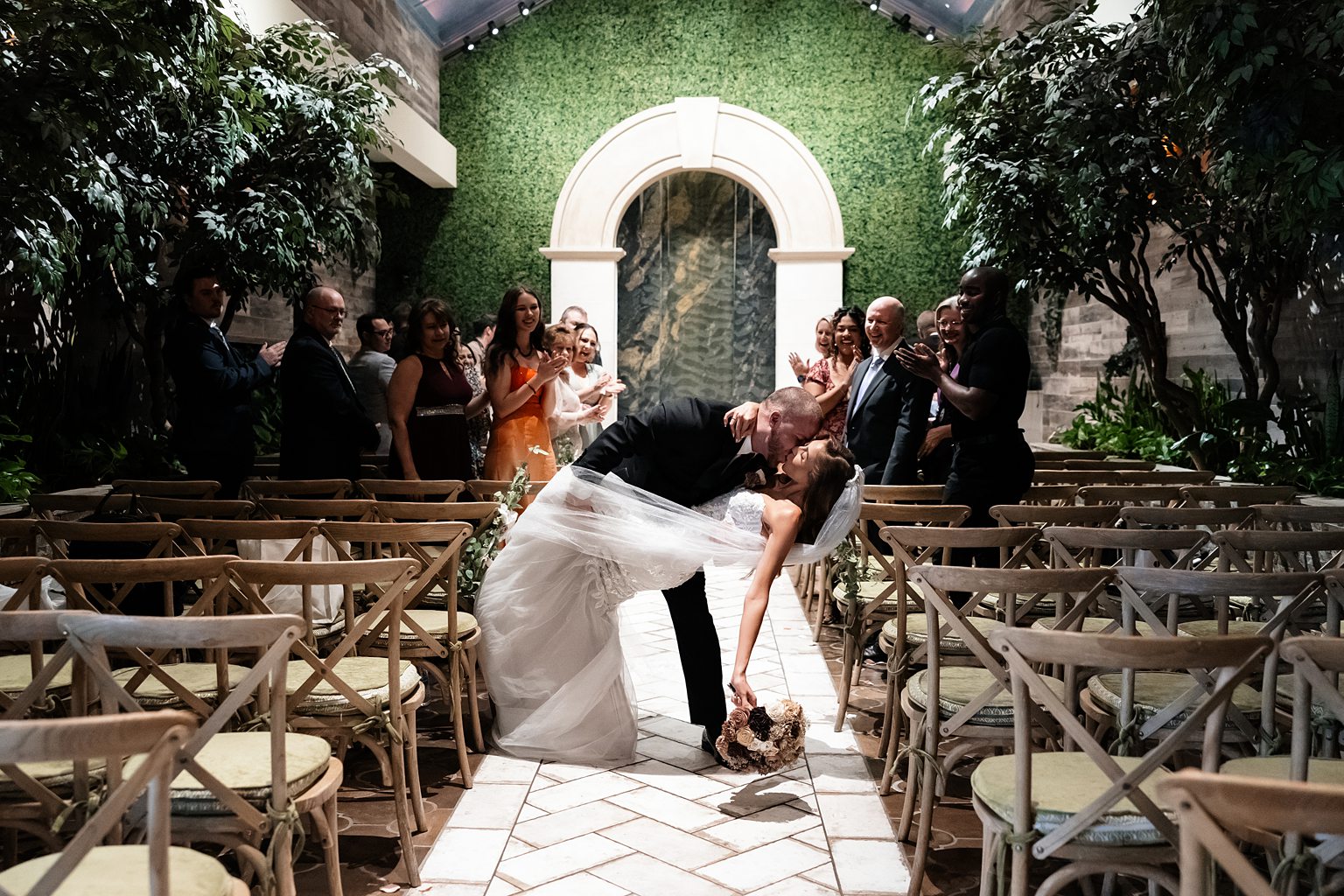 Bride and grooms end of aisle dip kiss during their Chapel of Flowers wedding ceremony in The Glass Gardens