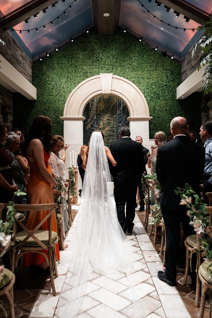 Bride being walked down the aisle by her father for her Chapel of Flowers Glass Gardens wedding ceremony