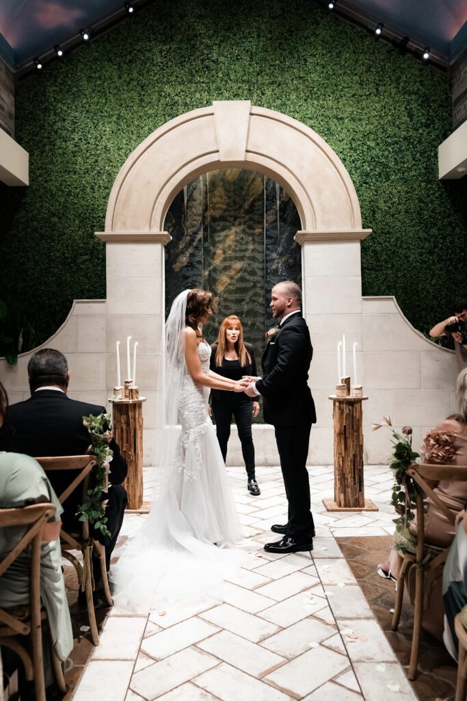 Bride and groom holding hands during their Chapel of Flowers wedding ceremony in The Glass Gardens