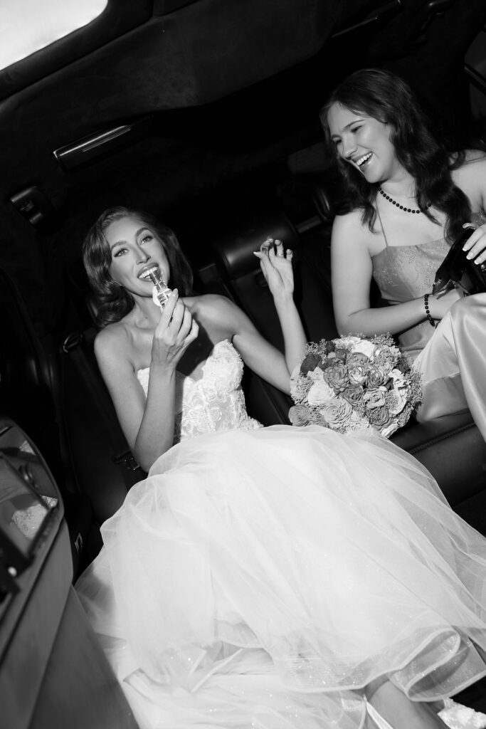 Black and white photo of a bride and her bridesmaids taking shots in a limo