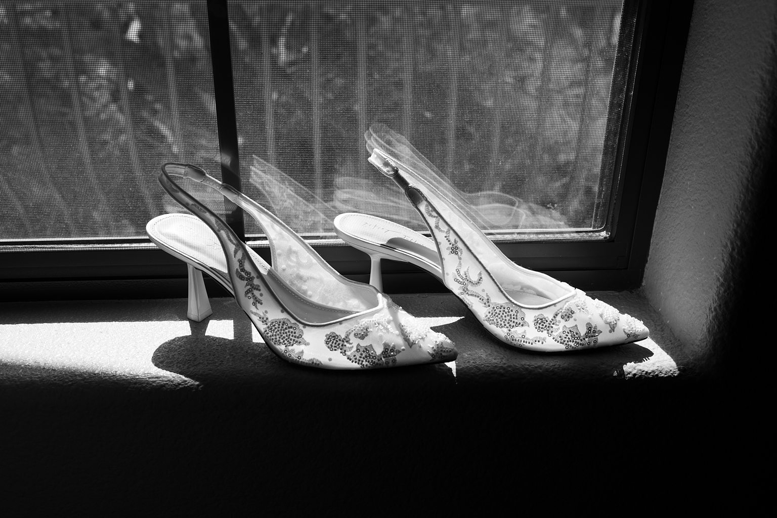 Black and white photo of a brides wedding shoes on a window edge