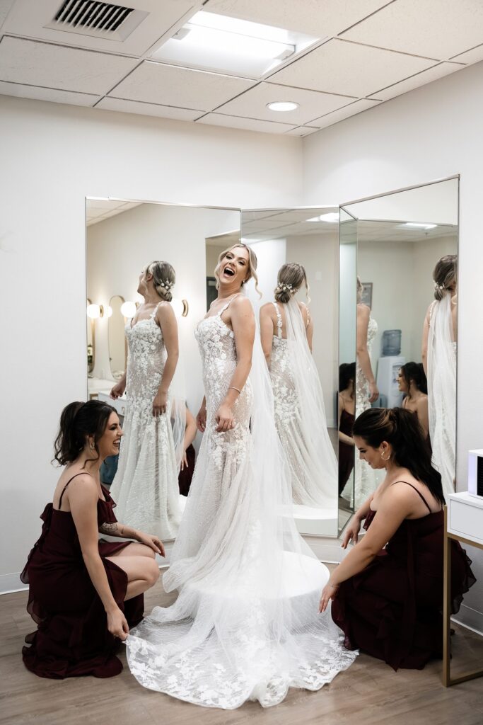 Bride laughing as the bridesmaids fix her veil and dress