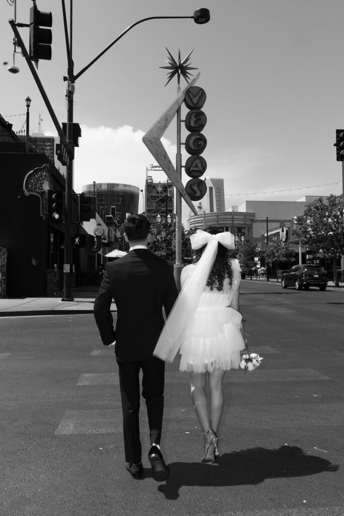 Bride and groom walking across the street by the Vegas sign on Fremont Street