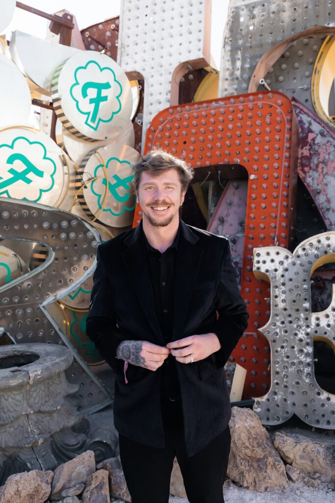 Groom posing for his Neon Museum wedding photos wearing a tailored black velvet suit