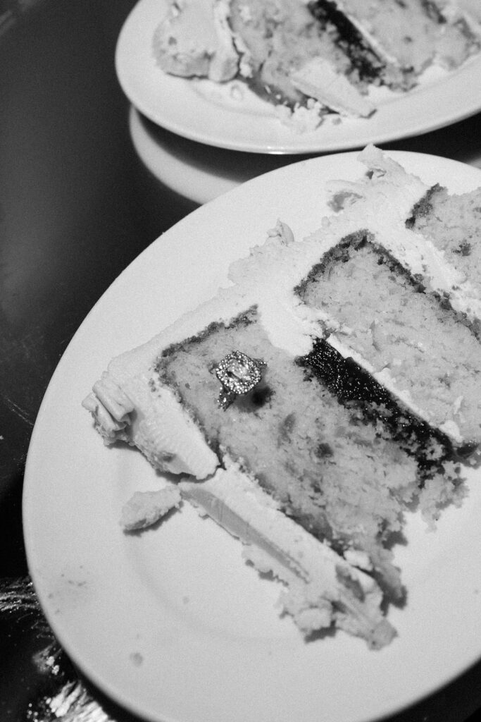 Black and white wedding reception detail shot with wedding cake slices and the brides ring in the cake