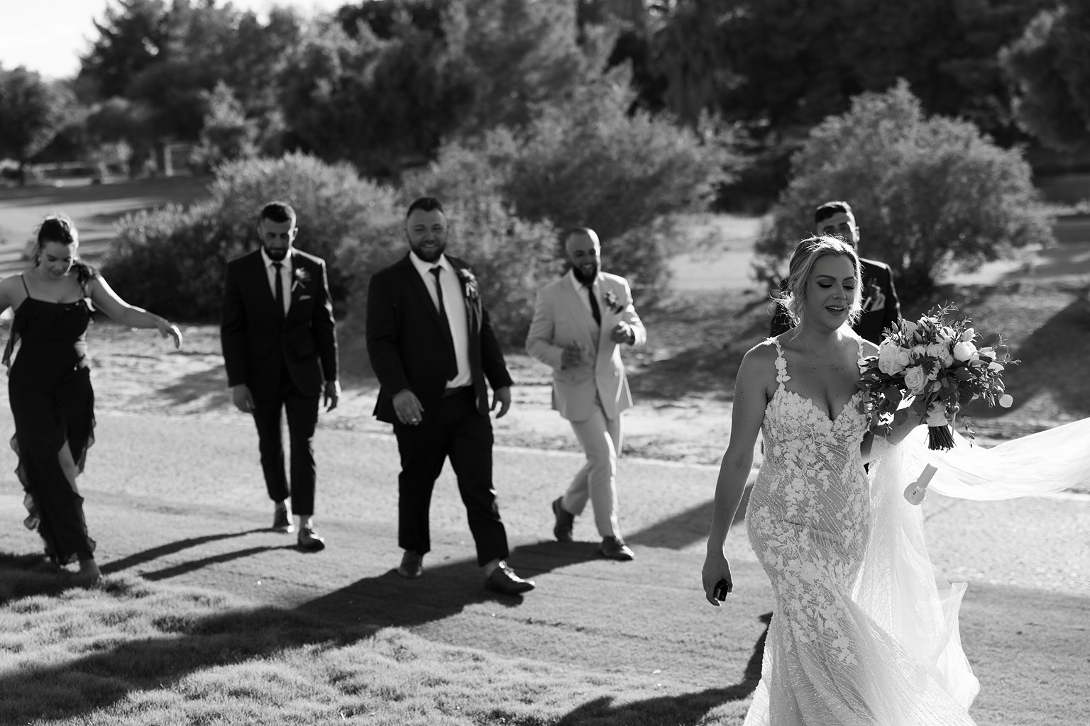 Black and white photo of a the wedding party walking out to the golf course for portraits