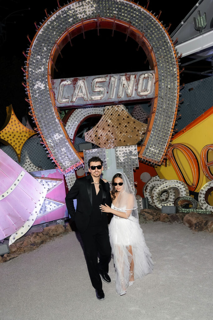 Bride and groom walking in front of a casino sign in the Neon Museum at night,