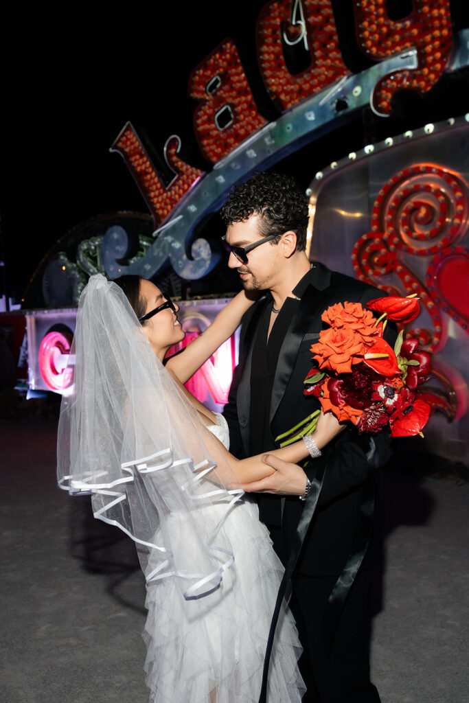 Bride and groom posing in front of the Lady Luck sign for their Neon Museum wedding photos at night.