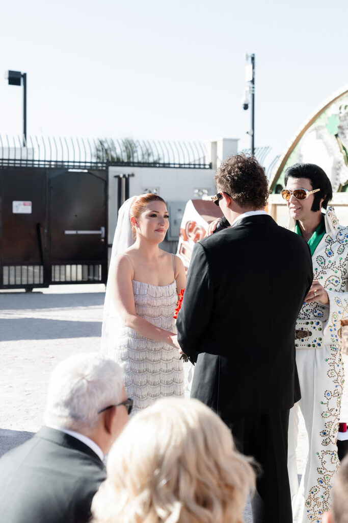 Bride and groom holding hands at the altar while their Elvis officiant speaks. 