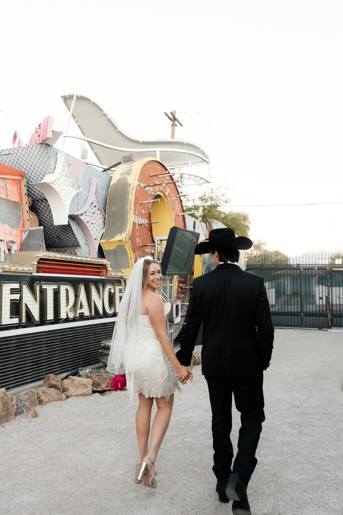 Bride and groom holding hands while walking through The Neon Museum.