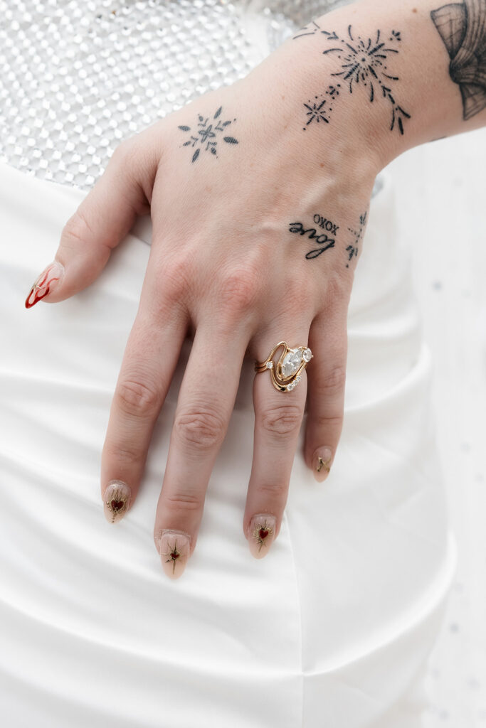 Close up shot of a brides hand resting on her dress and showing off her wedding ring.