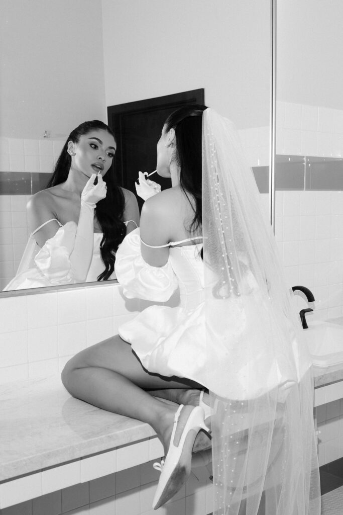 Black and white photo of a bride applying lipstick in the bathroom at That Chapel Downtown
