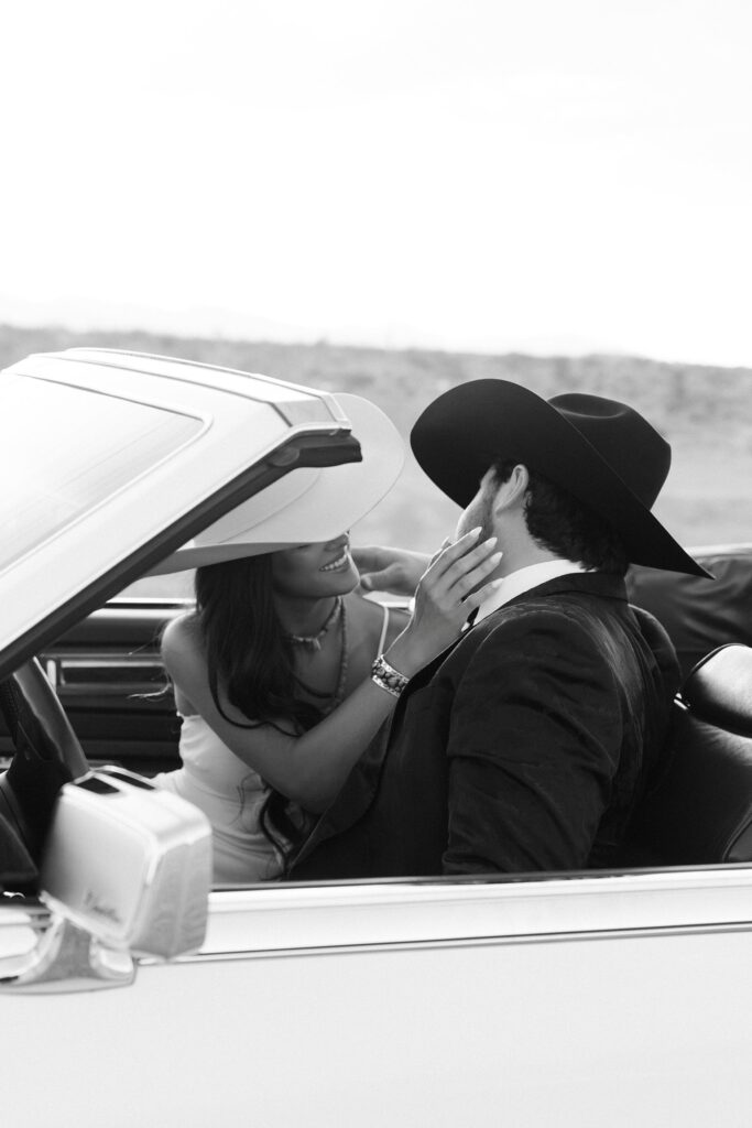 Black and white image of a couple sharing a moment in a vintage car during their western engagement photos in Las Vegas.