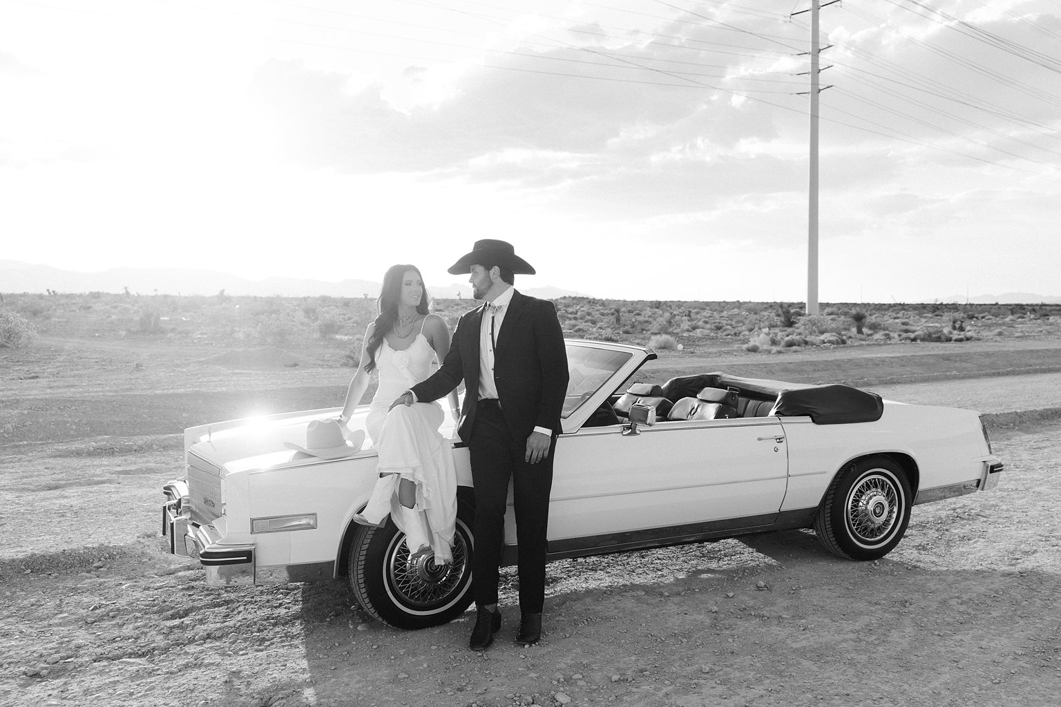 Golden hour engagement photos in Las Vegas with a couple sitting on a vintage Cadillac, dressed in modern western fashion.
