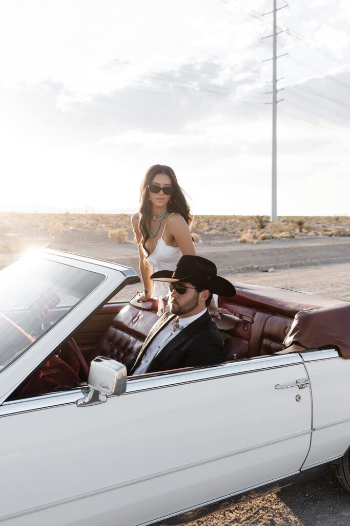 Couple wearing sunglasses and posing in a white Cadillac Eldorado for their western engagement photos in Las Vegas near Lee Canyon
