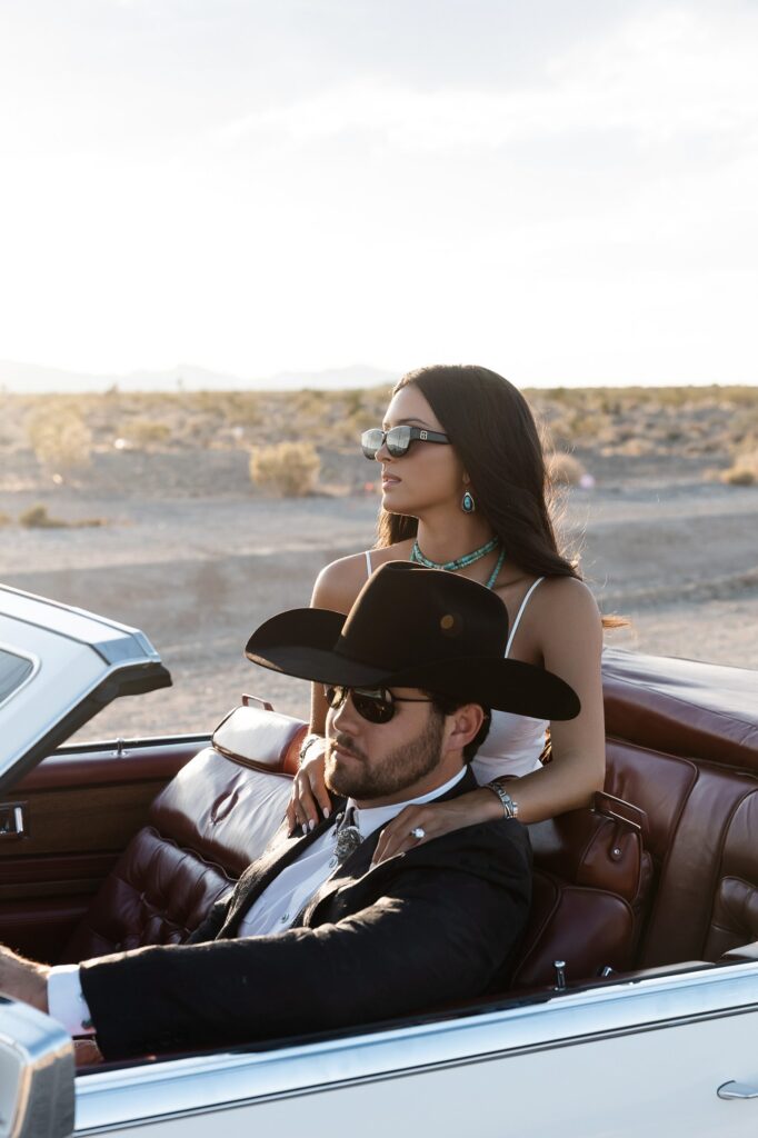 Couple wearing sunglasses and posing in a white Cadillac Eldorado for their western engagement photos in Las Vegas near Lee Canyon