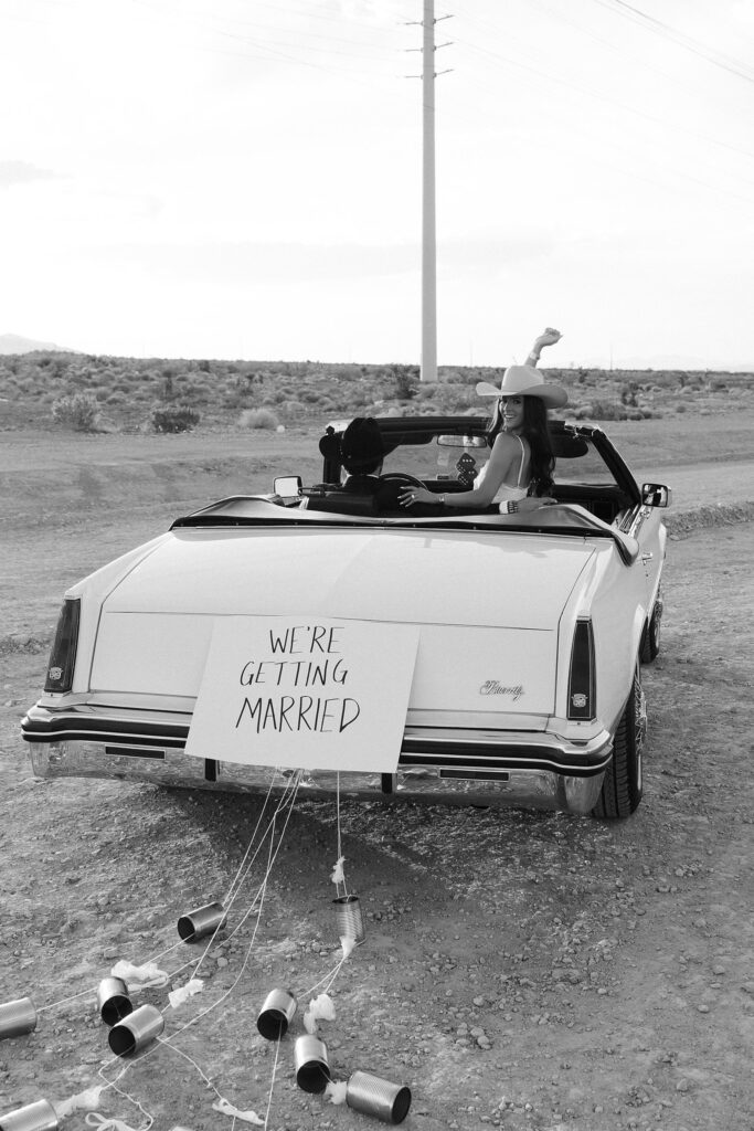 Black and white photo of a couple riding off in a car and a "We're Getting Married" sign on the back