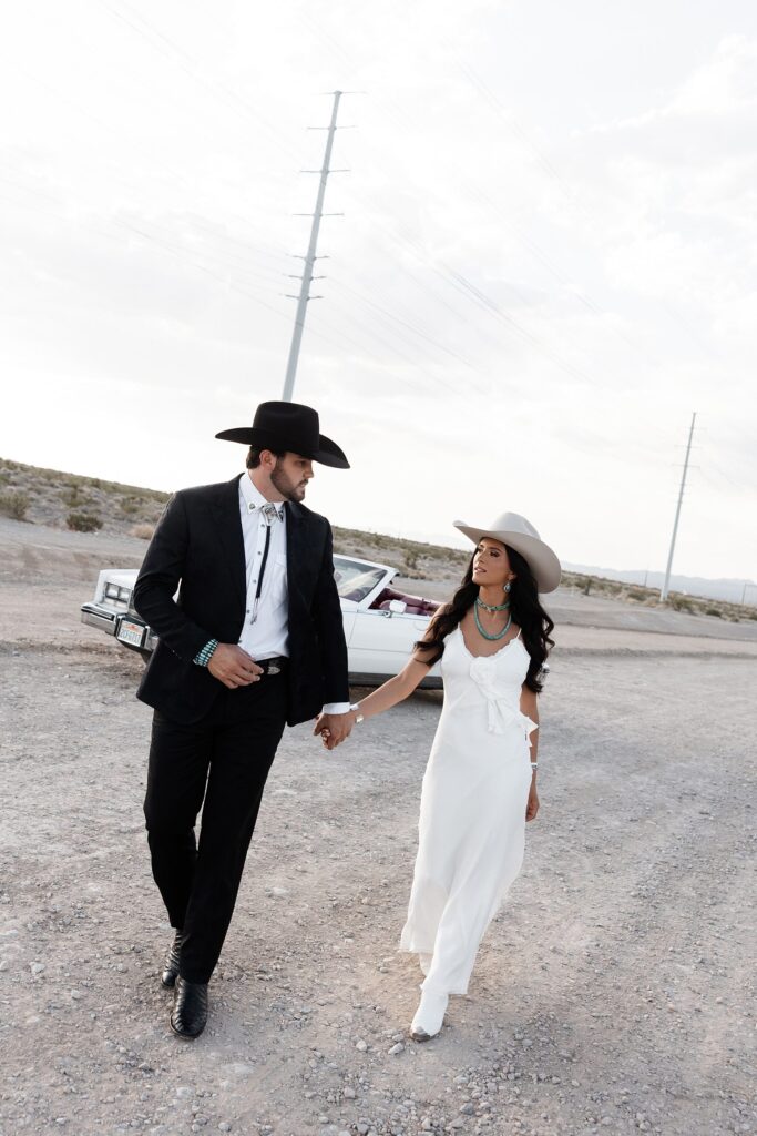 Couple walking away from a vintage Cadillac during their engagement photos in Las Vegas with desert views all around.

