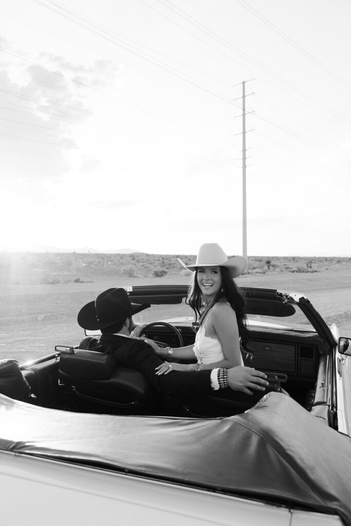 Black and white photo of an engaged couple posing in a car