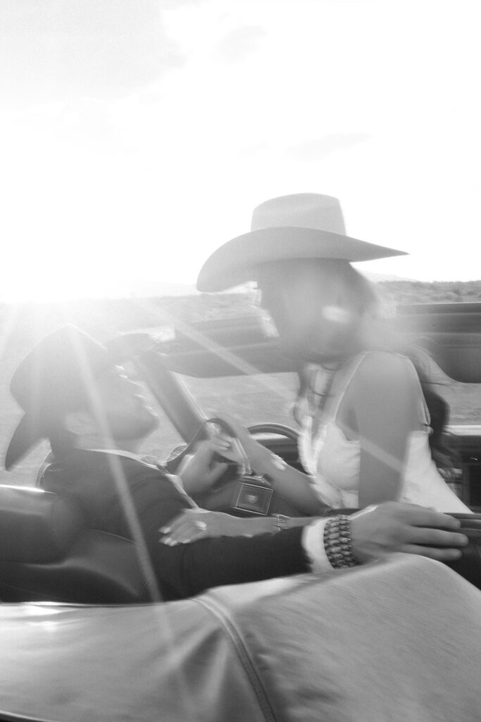 Blurry black and white golden hour engagement photo of a western couple in a car