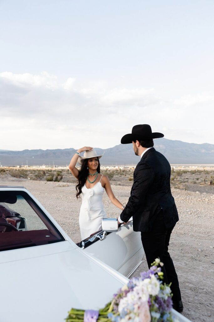 Las Vegas engagement session with a couple posing near a vintage white Cadillac, dressed in sleek, fashion-forward western outfits.