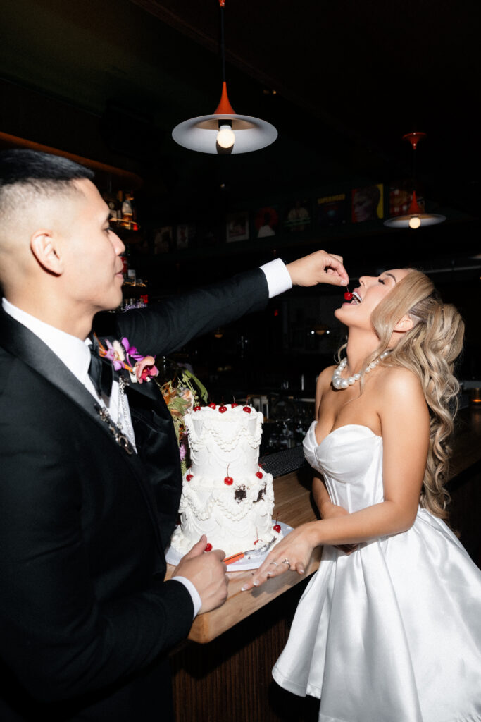Groom feeding the bride a cherry off of their cake.