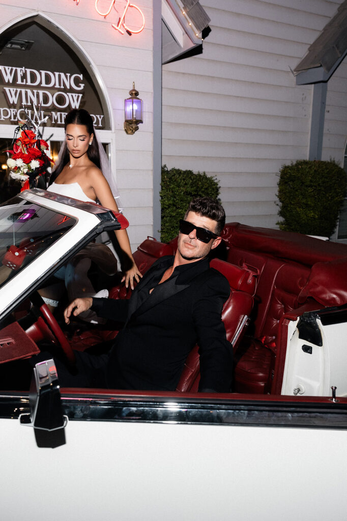 Robin Thicke and April Love Geary posing in a classic car in front of A Special Memory Wedding Chapel